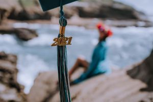 Graduation tassels blow in the wind against a blurred coastal background.