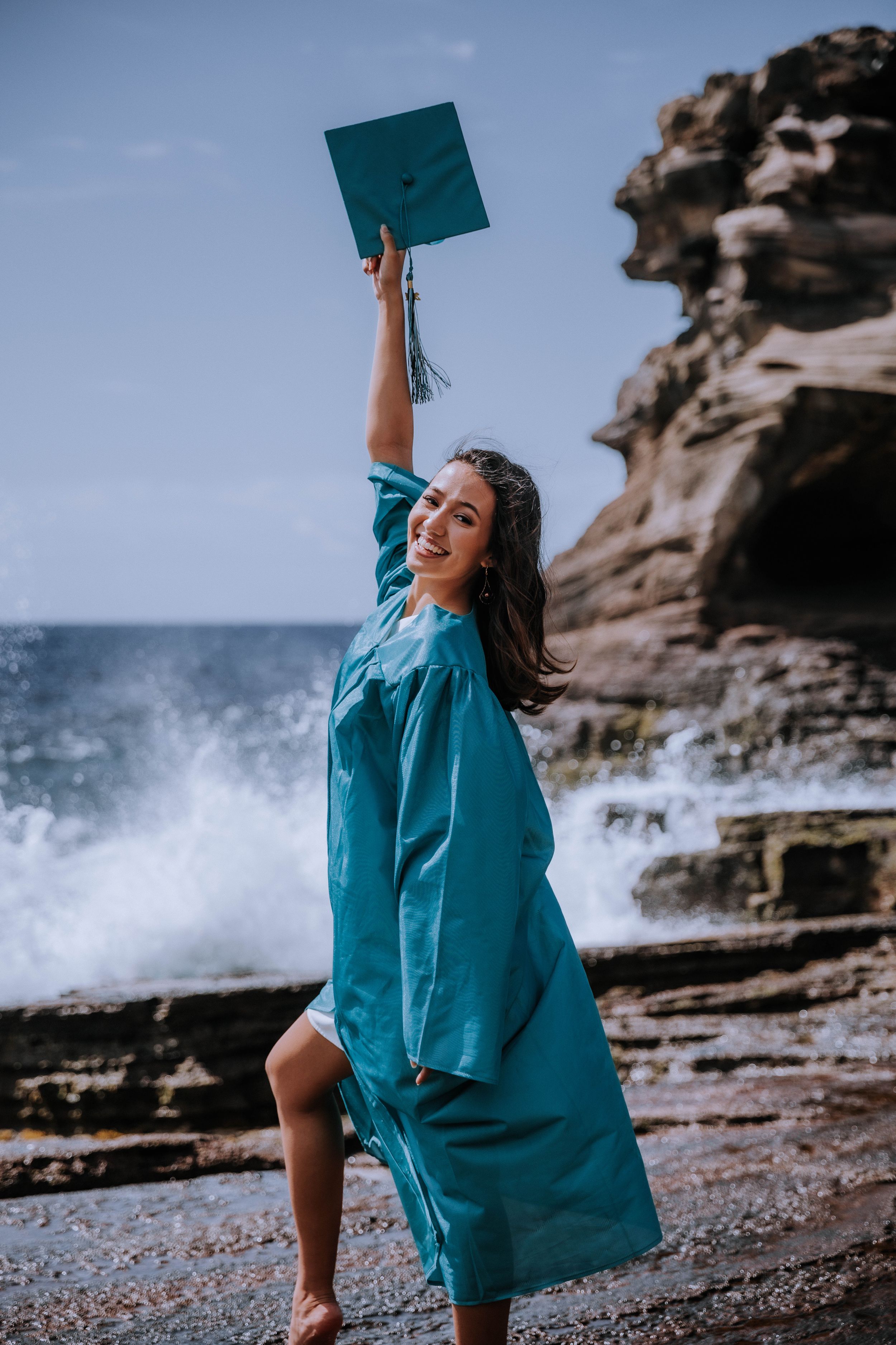 A joyful graduation photo session on a rocky beach with waves crashing in the background.