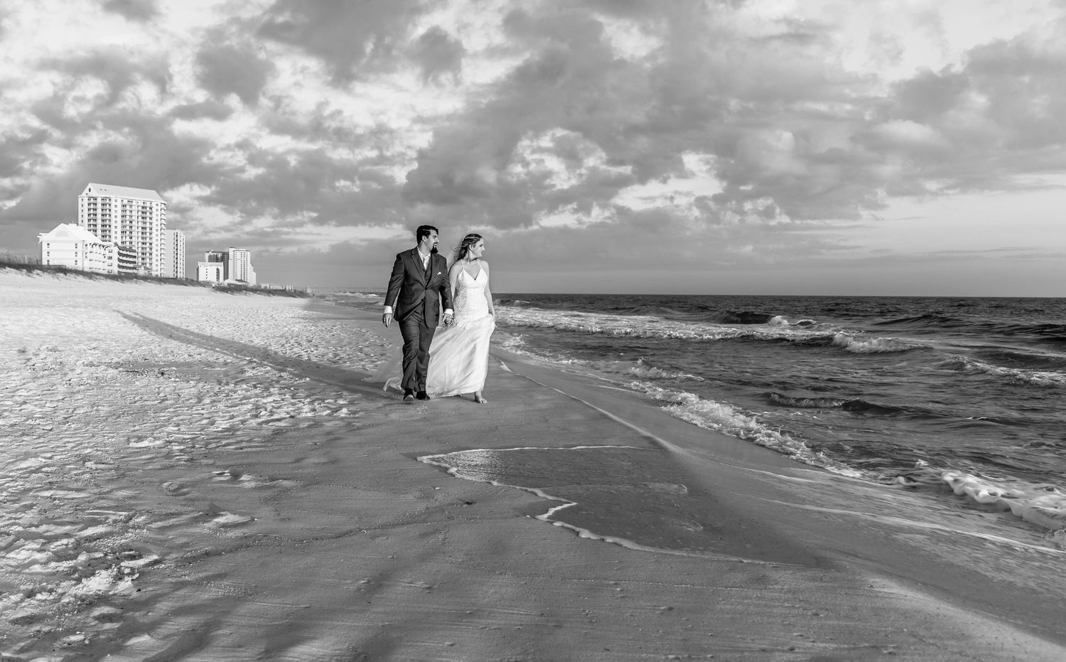Black and white beach wedding photo with waves and condos in background.