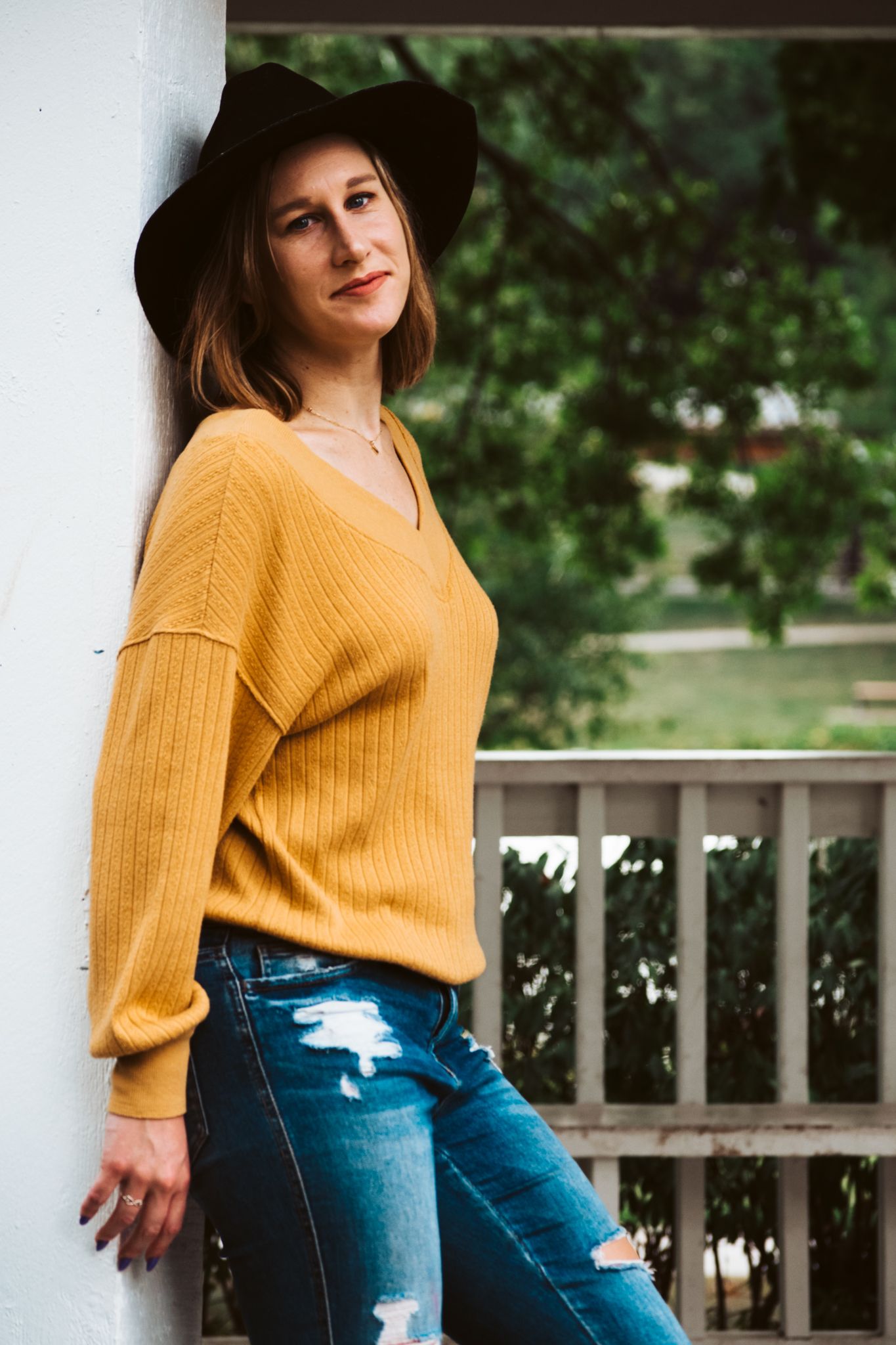 Portrait Session. Young adult woman stands against a gazebo and smirks at the camera.