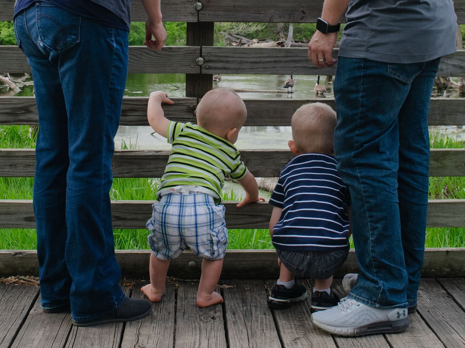 Family portrait session. Two boys on bridge between parents. Craig Crossing Park, Lenexa, KS