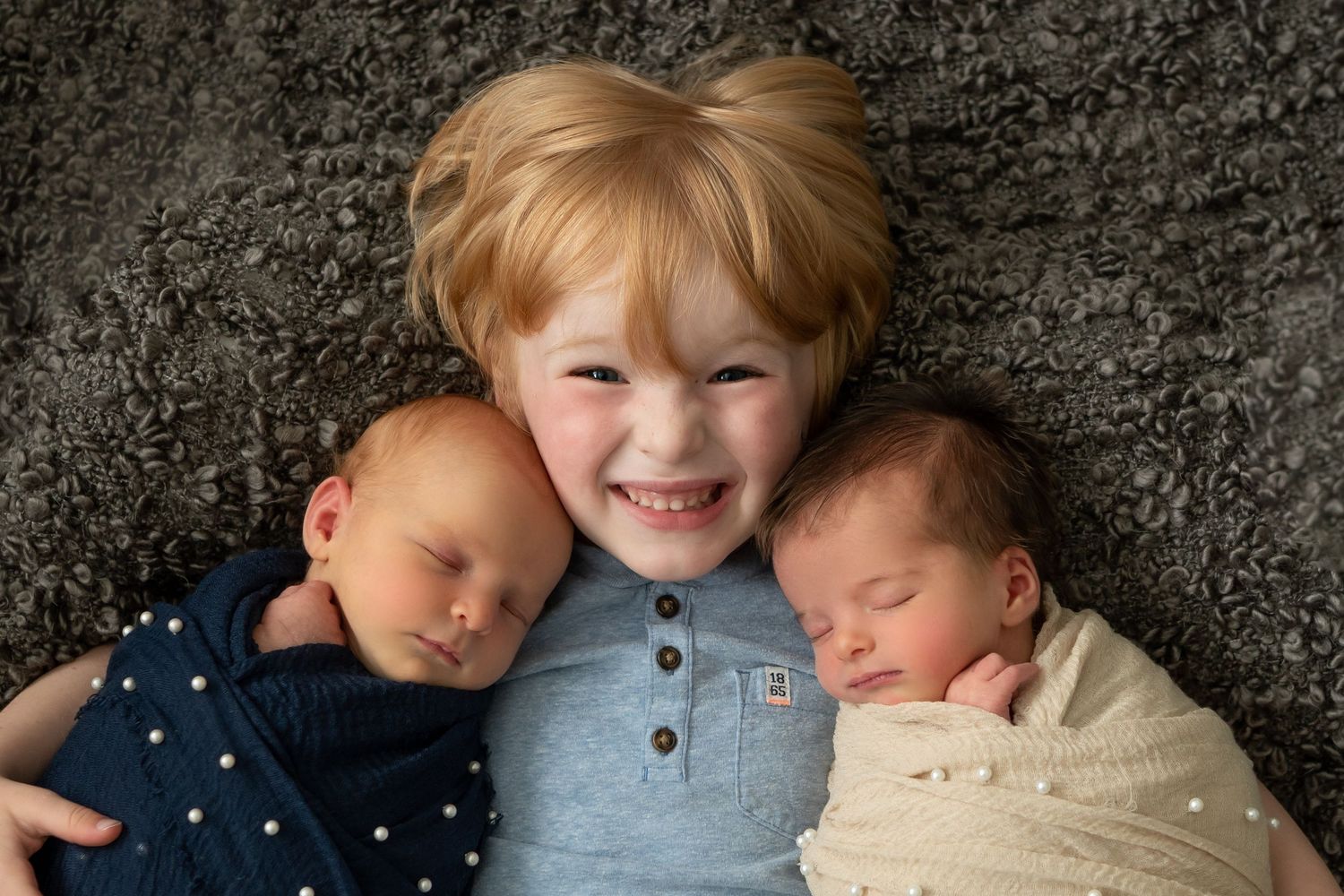Children cuddling together on dark textured background during portrait session.