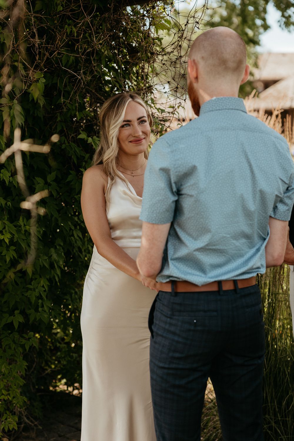 A couple shares an intimate moment in an outdoor garden setting wearing formal attire.