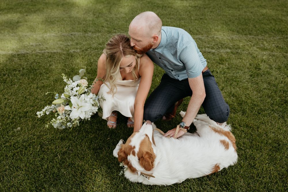 A couple kneels down to pet their beloved dog during their special day.