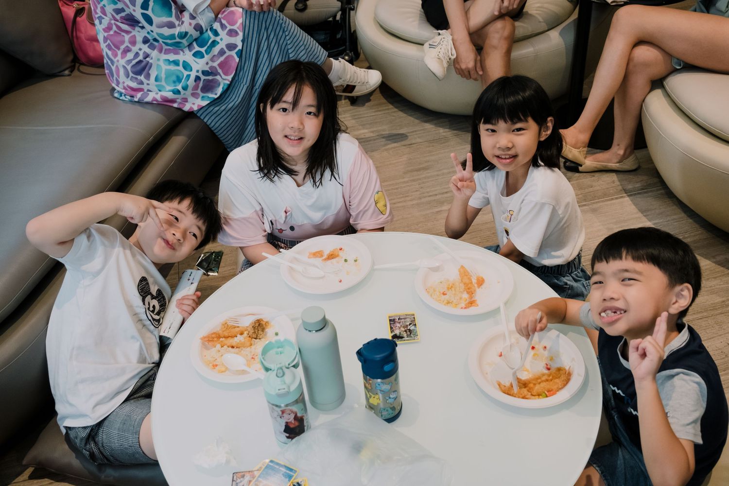 Children sit around a white table with drinks and snacks during a casual gathering.