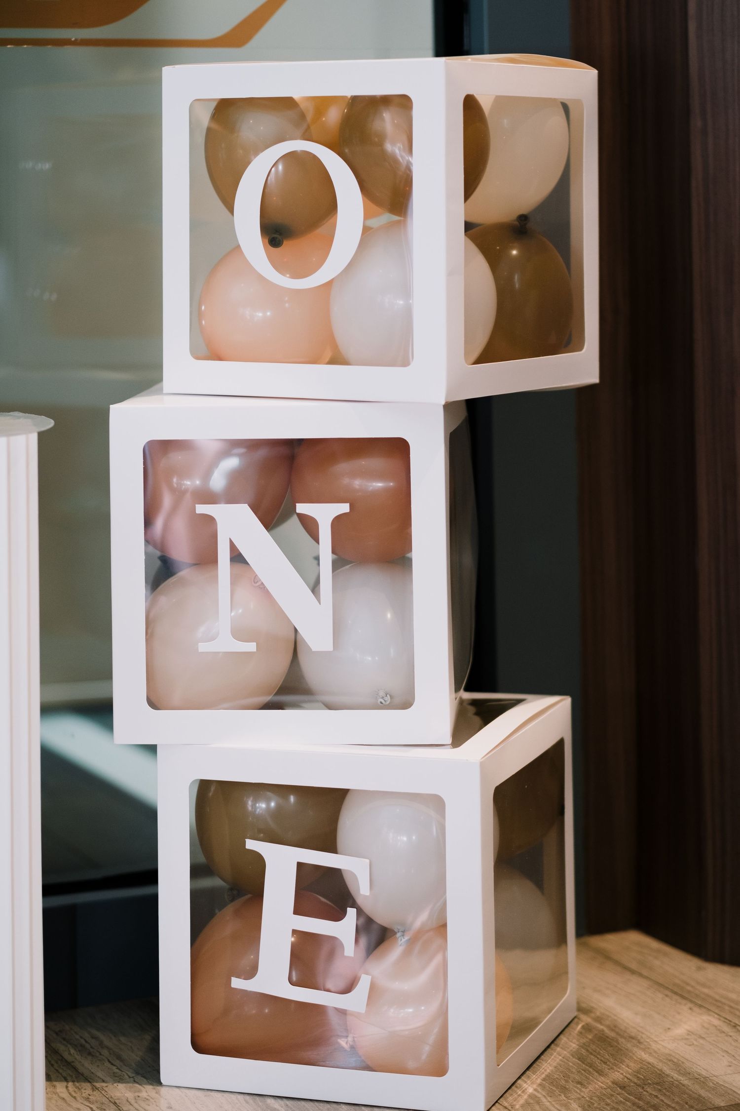 White decorative cube boxes spelling 'ONE' with balloons in background.