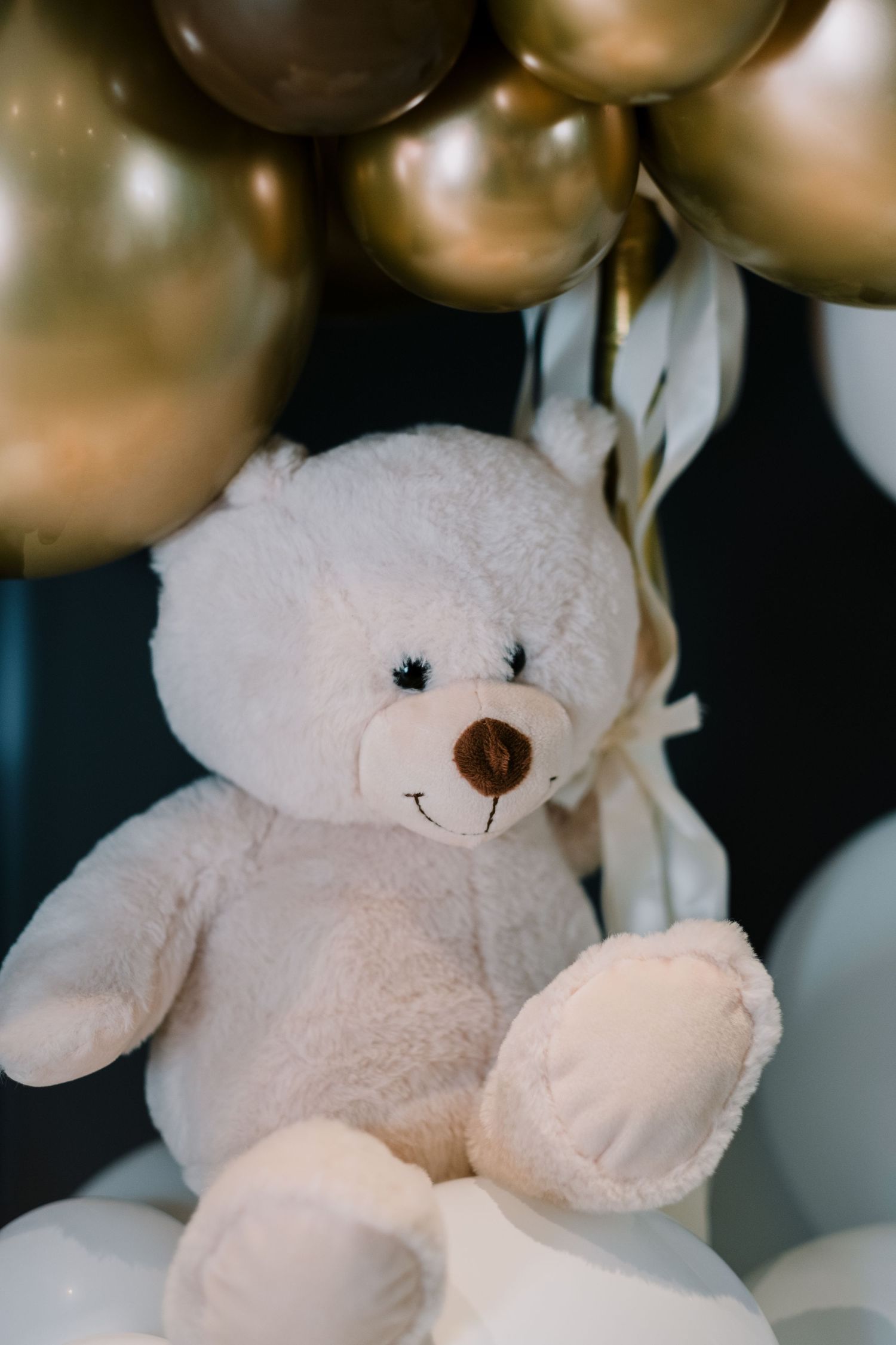 White plush teddy bear with gold balloons in background.