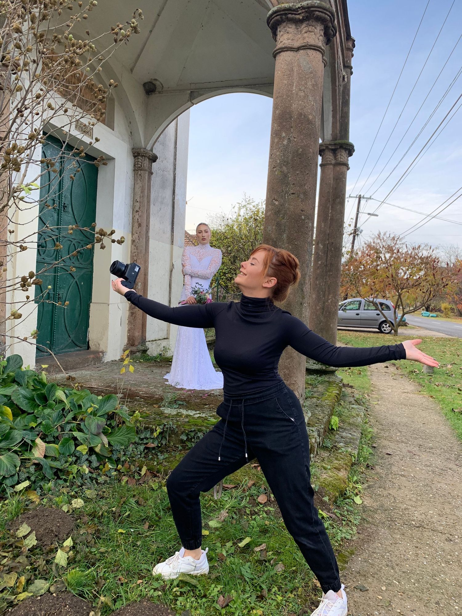 Person in black outfit striking dramatic pose under architectural archway outdoors.