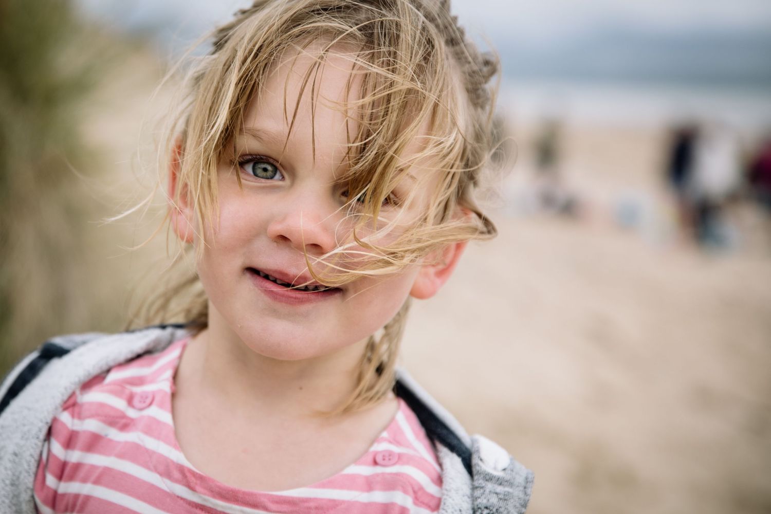 Windswept hair and a bright smile on a cloudy beach day.