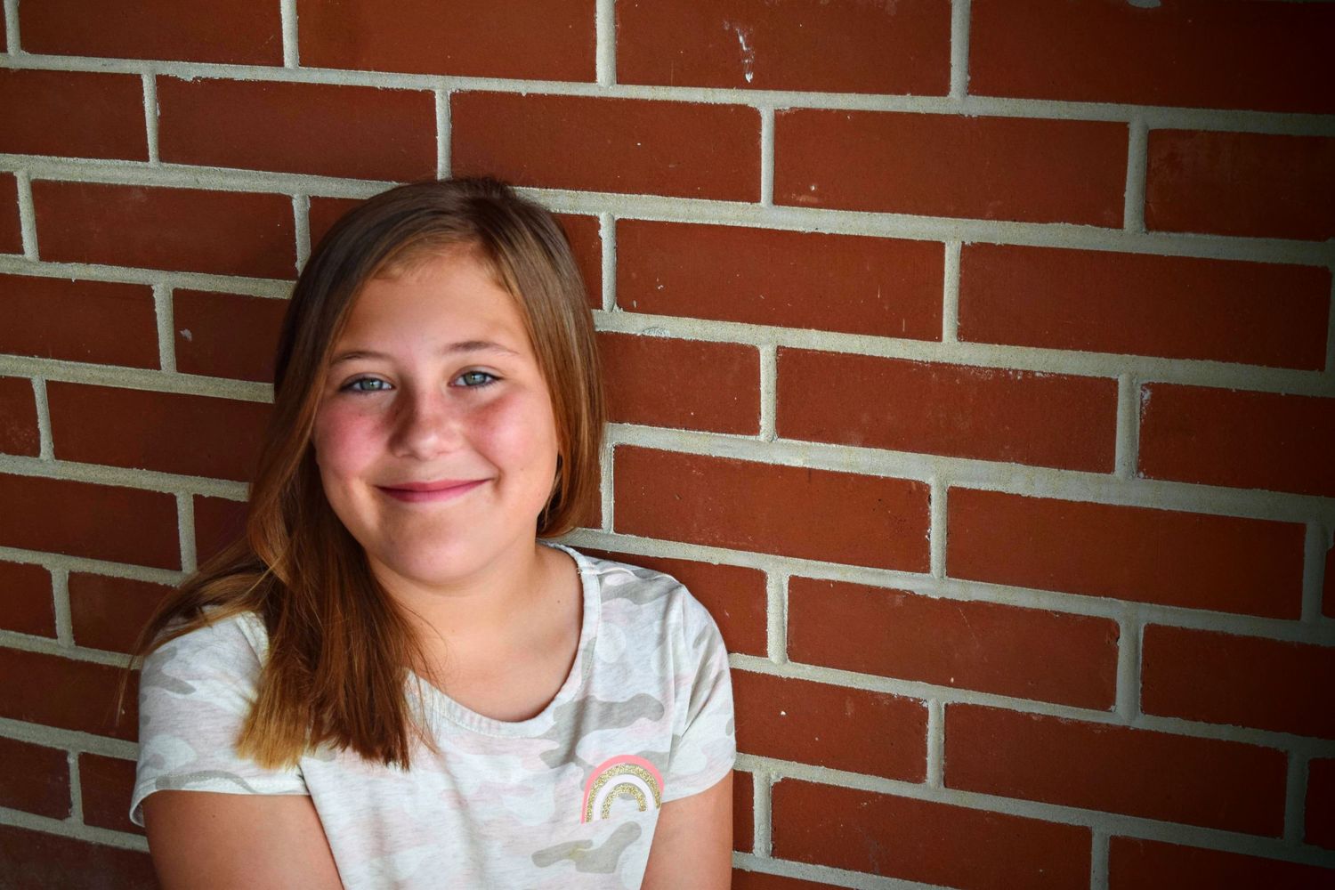 Headshot Session. Teenaged model sits in front of a brick wall and smiles at the camera. Downtown Olathe, KS