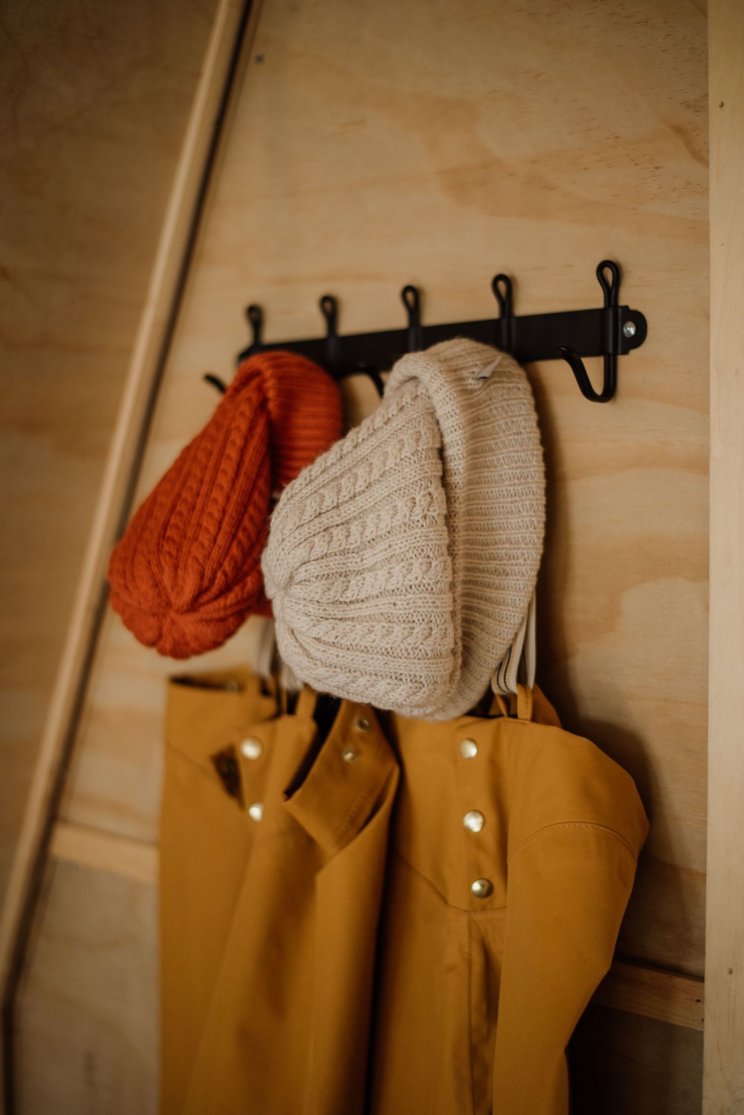 Orange and cream knit beanies hanging on wall hooks above mustard yellow outerwear.