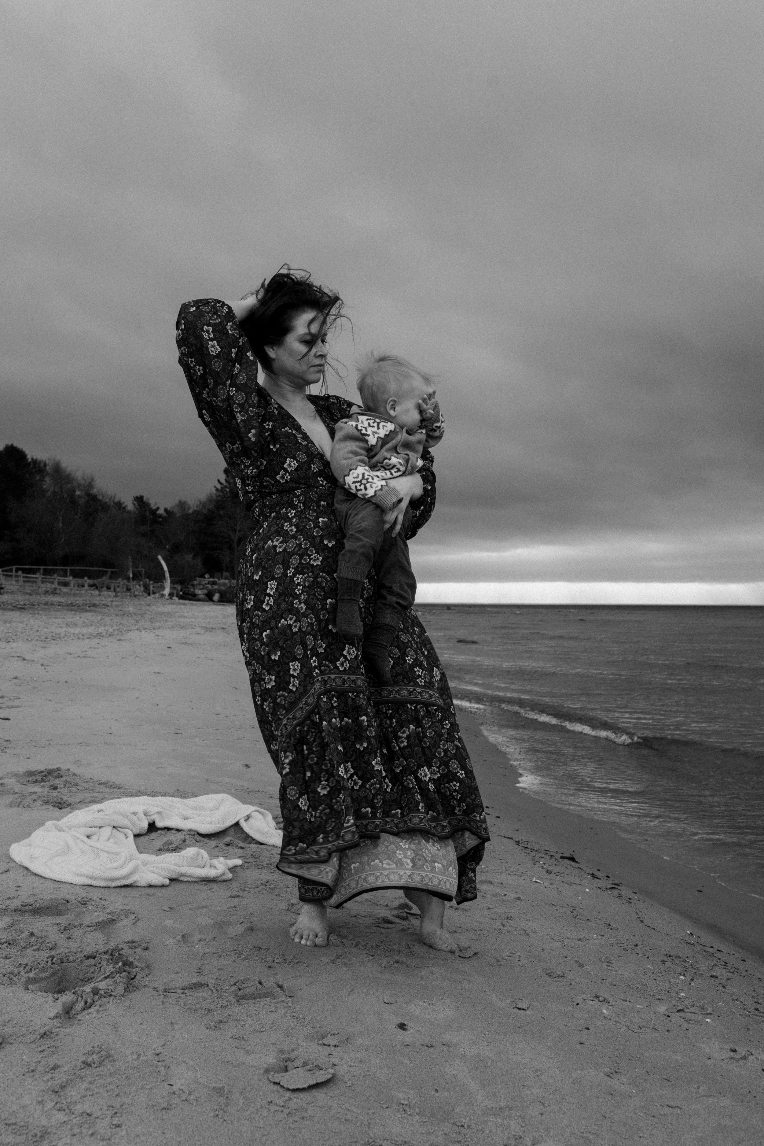 A flowing dress catches the wind as figures embrace on a moody beach at sunset.