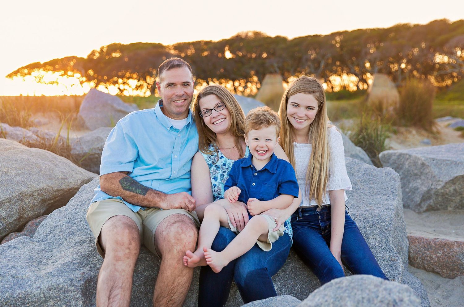 A family sits together on coastal rocks during golden hour at the beach.