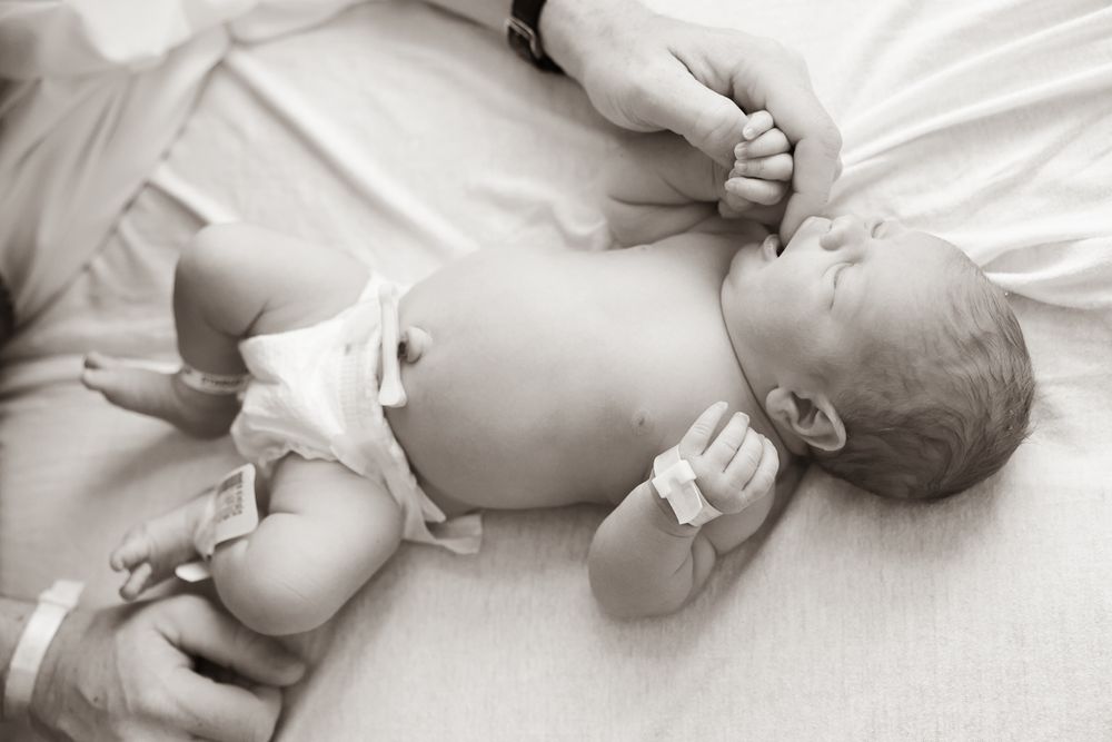 Peaceful newborn baby resting on white bedding in black and white photo.