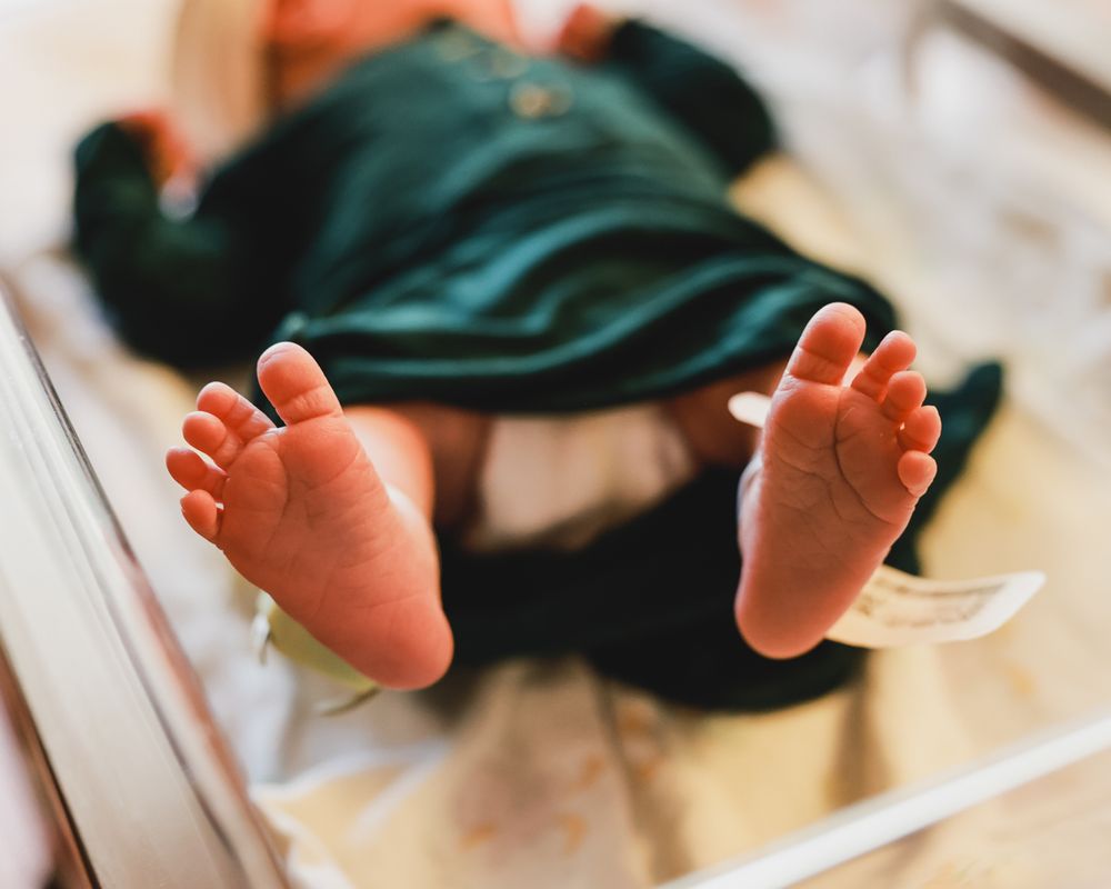Close-up of tiny baby feet in green clothing on white surface.