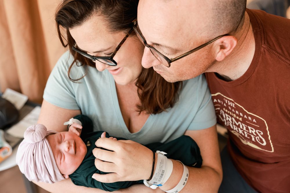 Parents lean in close to admire their newborn baby wrapped in soft clothing.