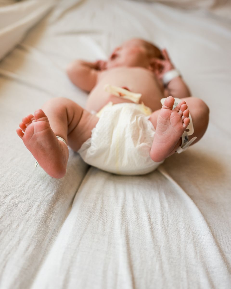 Tiny newborn baby feet and diaper against white bedding in natural light.