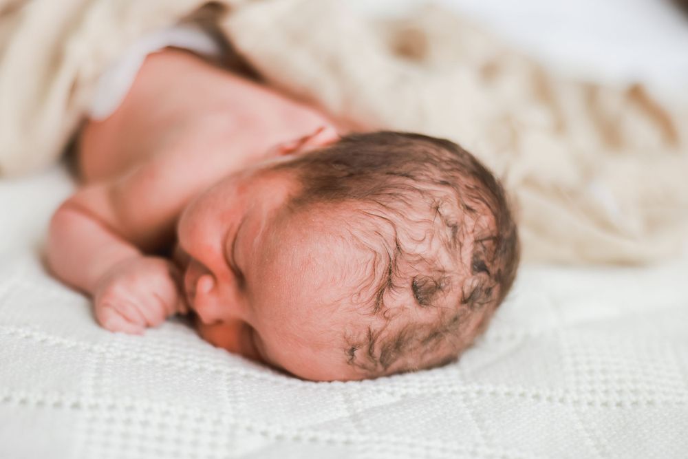 Close-up of a sleeping newborn baby with wet hair resting on white bedding.