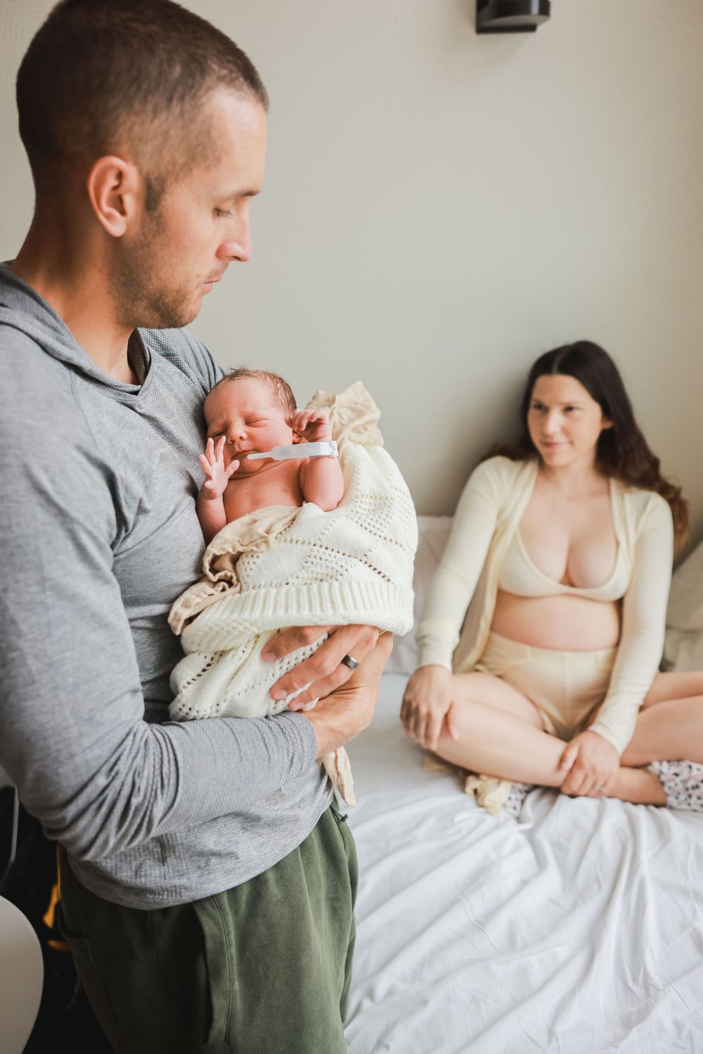 dad holding newborn in hospital with mom in the background