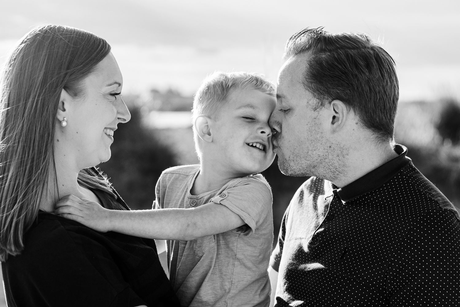 On a beach on Hayling Island, parents hold their three year old son close smiling and laughing in the sunlight.