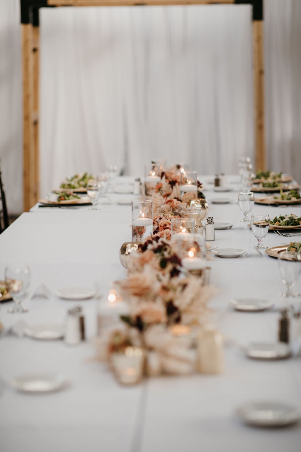 Elegant long reception table set with candles, blush floral centerpieces, and white linens.