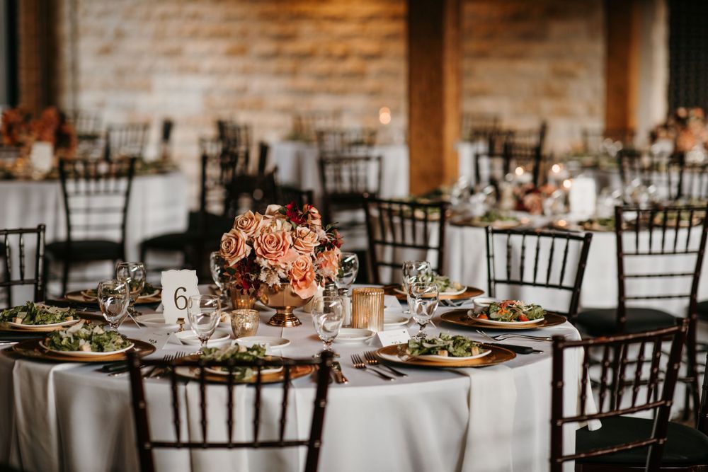 Round wedding reception tables set with dark chairs, lush floral centerpieces, and candlelight.