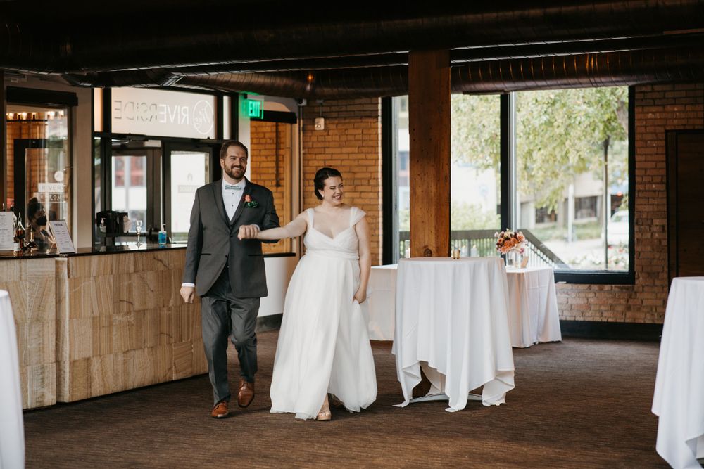 Bride and groom entering their wedding reception venue with brick walls and large windows.