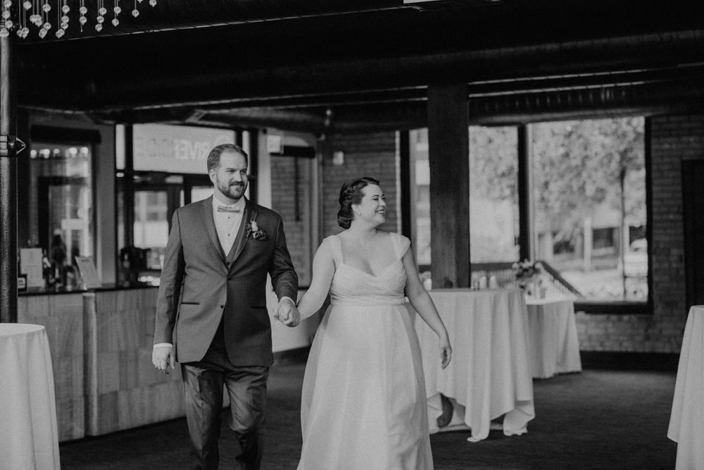 Black and white photo of bride and groom holding hands and smiling at wedding reception.