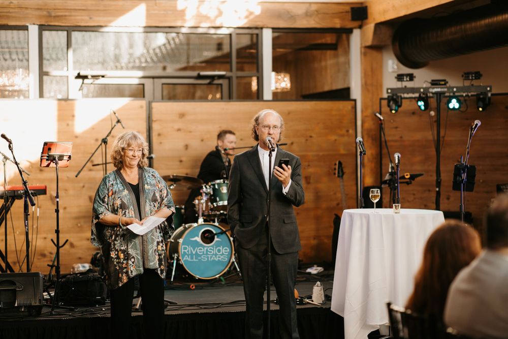 Couple giving a wedding toast speech with a live band performing in the background.