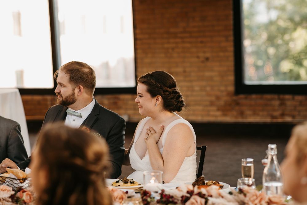 Bride and groom smiling and laughing while seated at their wedding reception head table.