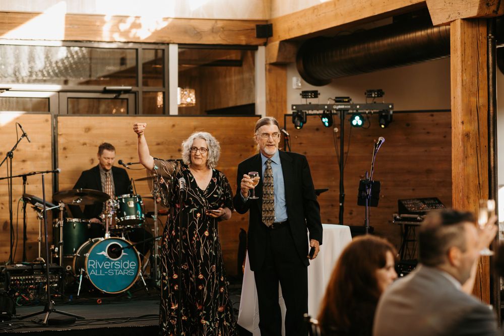 Smiling couple posing together at wedding reception with live band performing behind them.