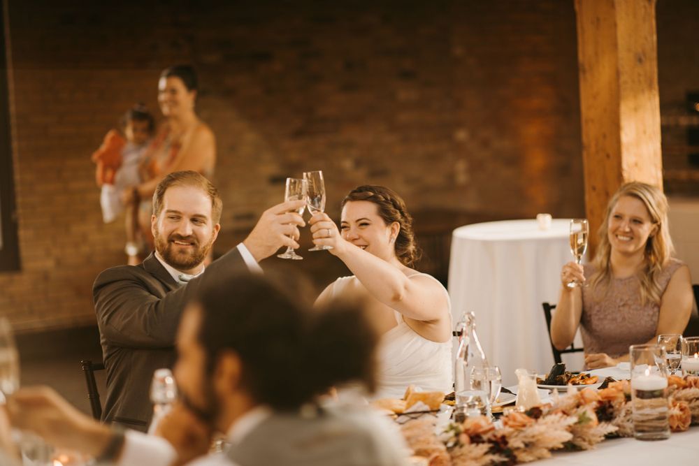 Smiling bride and groom raise champagne glasses in a toast at their elegant wedding reception.