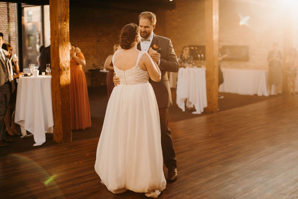 Newlyweds share their first dance in a warmly lit rustic wedding reception venue.