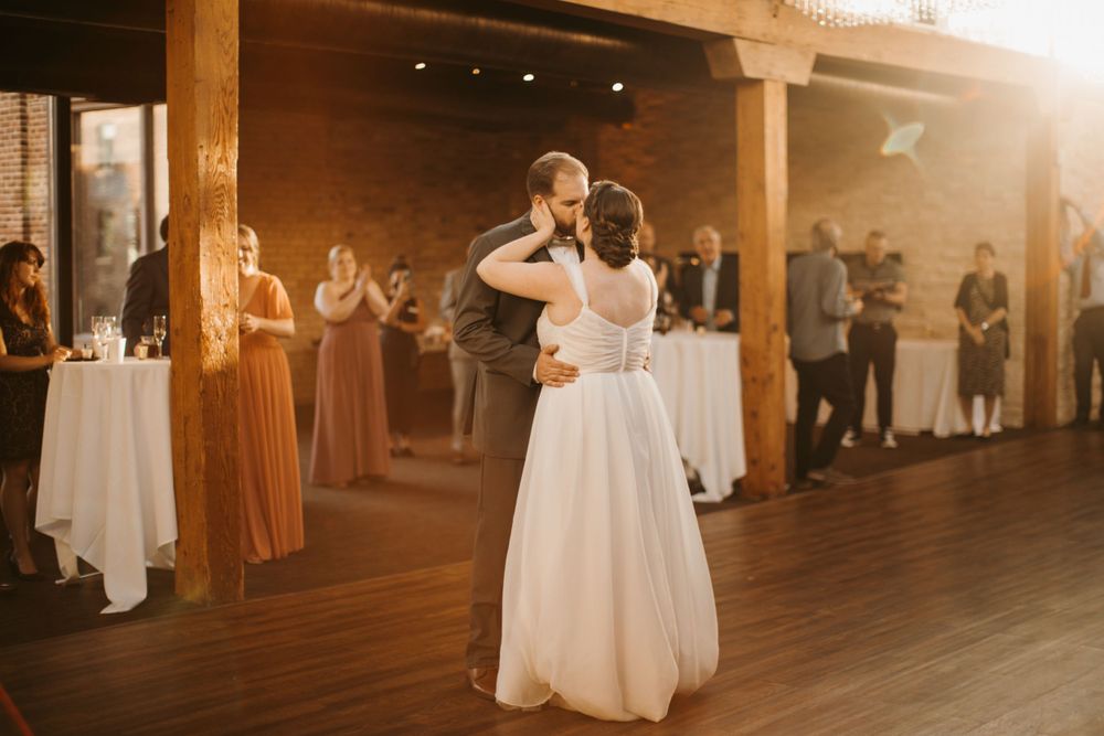 Newlyweds share a kiss during their first dance bathed in golden sunset light at reception.