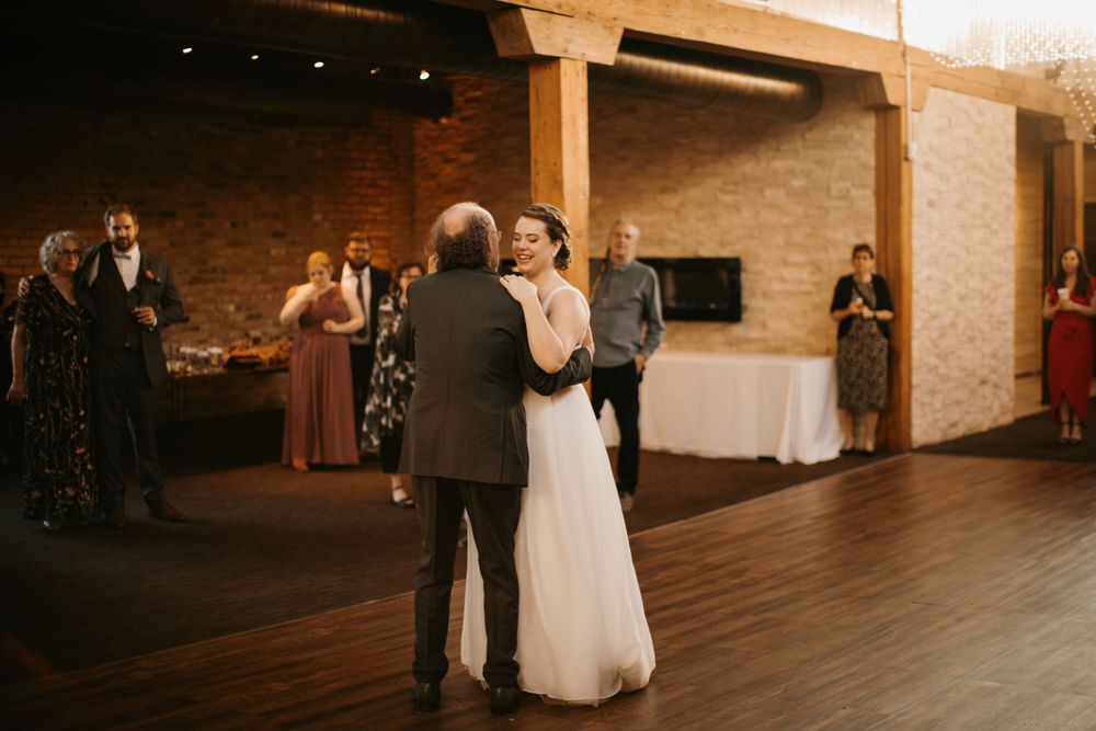 Bride smiles warmly while dancing with family member at elegant rustic wedding reception.