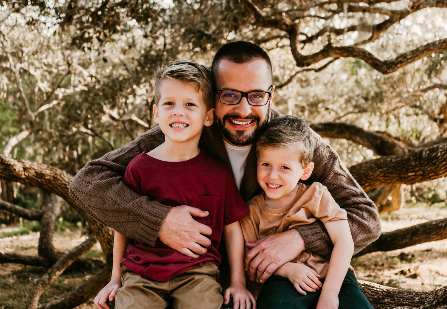 Outdoor Family Session Philippe Park in Safety Harbor, FL; Father and sons embracing in a tree at sunset