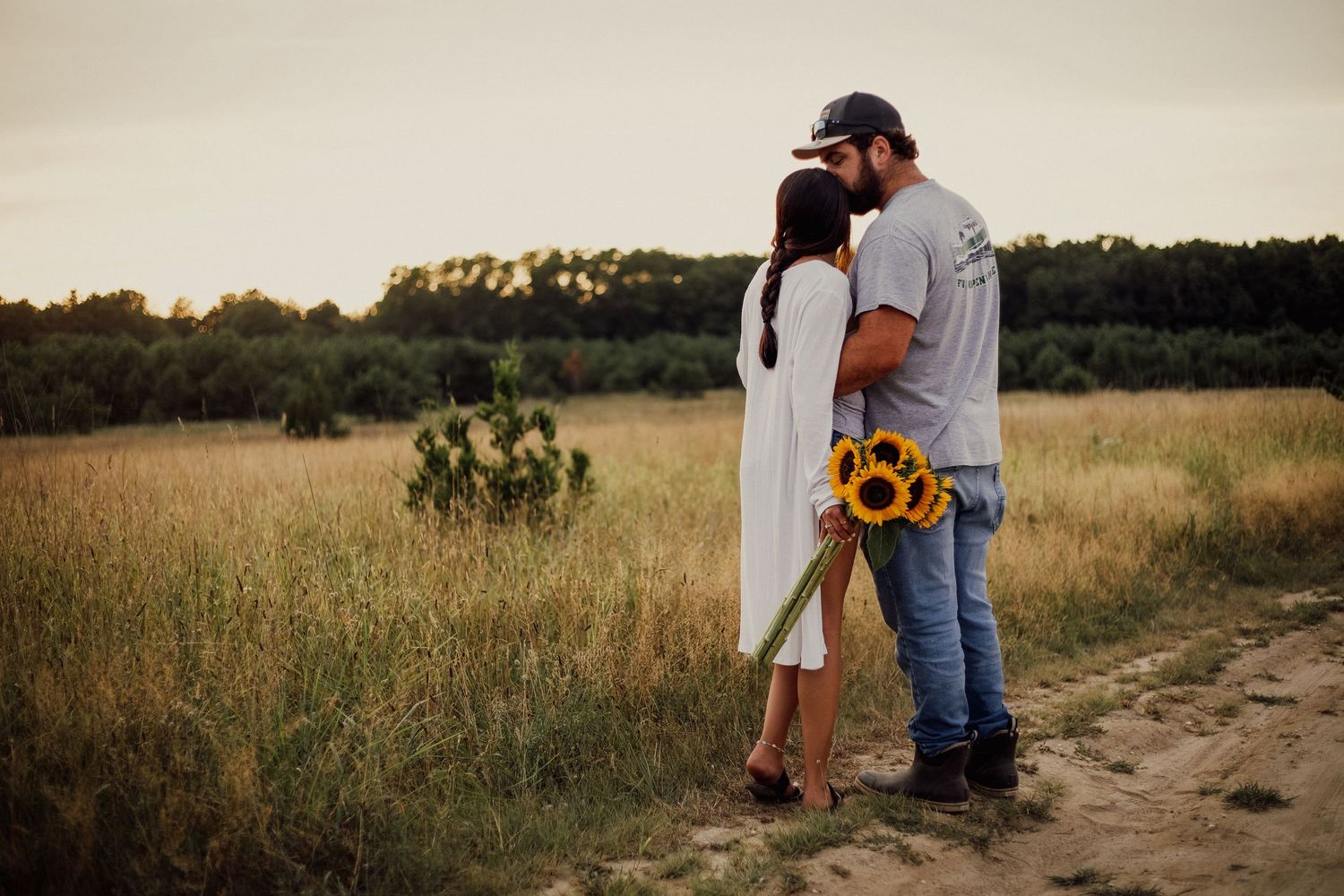 Two people standing on dirt path with sunflowers at golden hour.