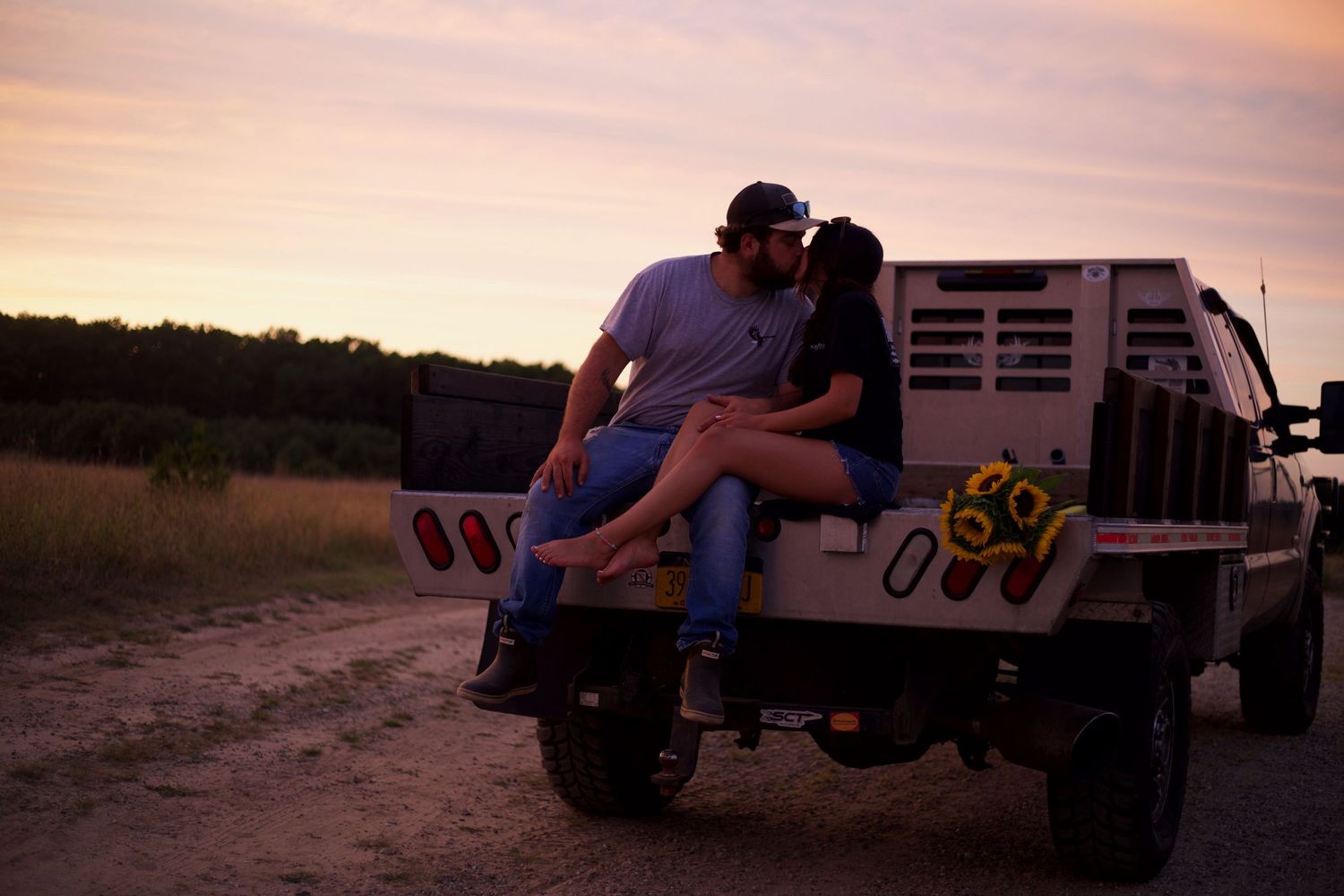 Silhouettes sitting on tailgate of truck during colorful sunset.