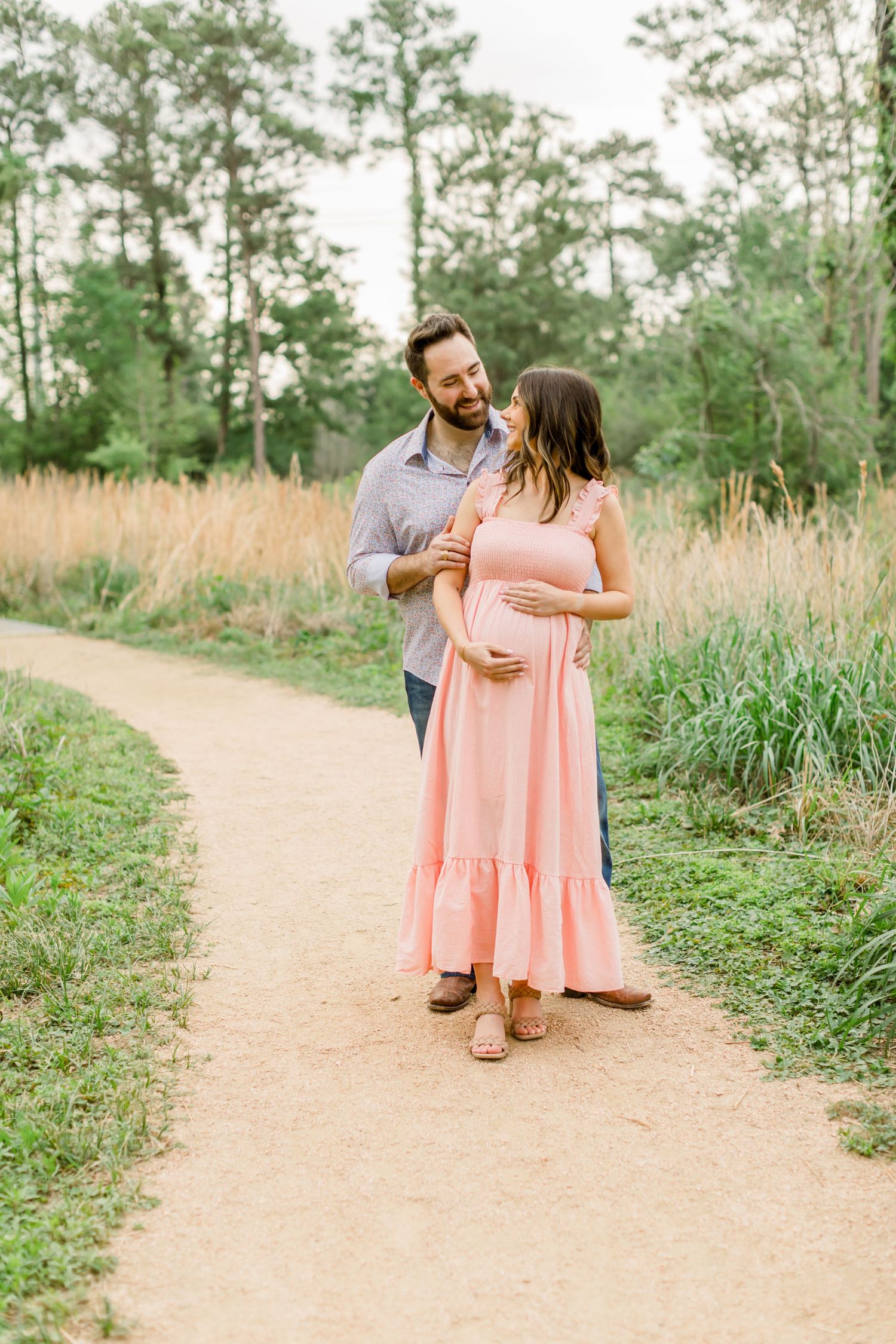 A tender embrace on a winding trail with tall grasses and pine trees in the background.