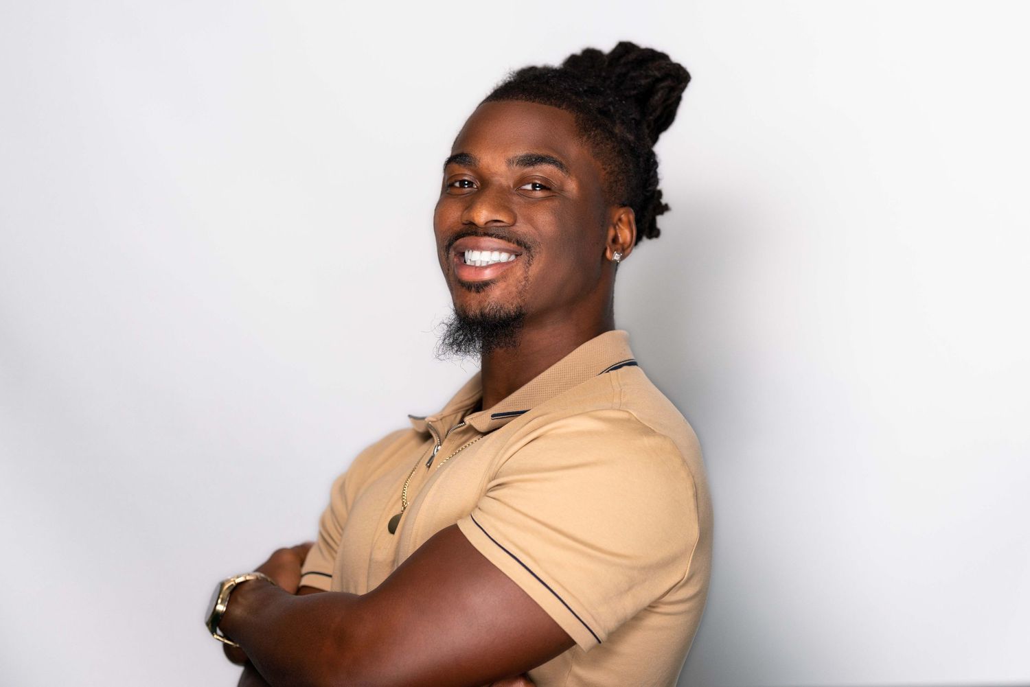 Studio portrait of person smiling in tan polo shirt with arms crossed against white background.