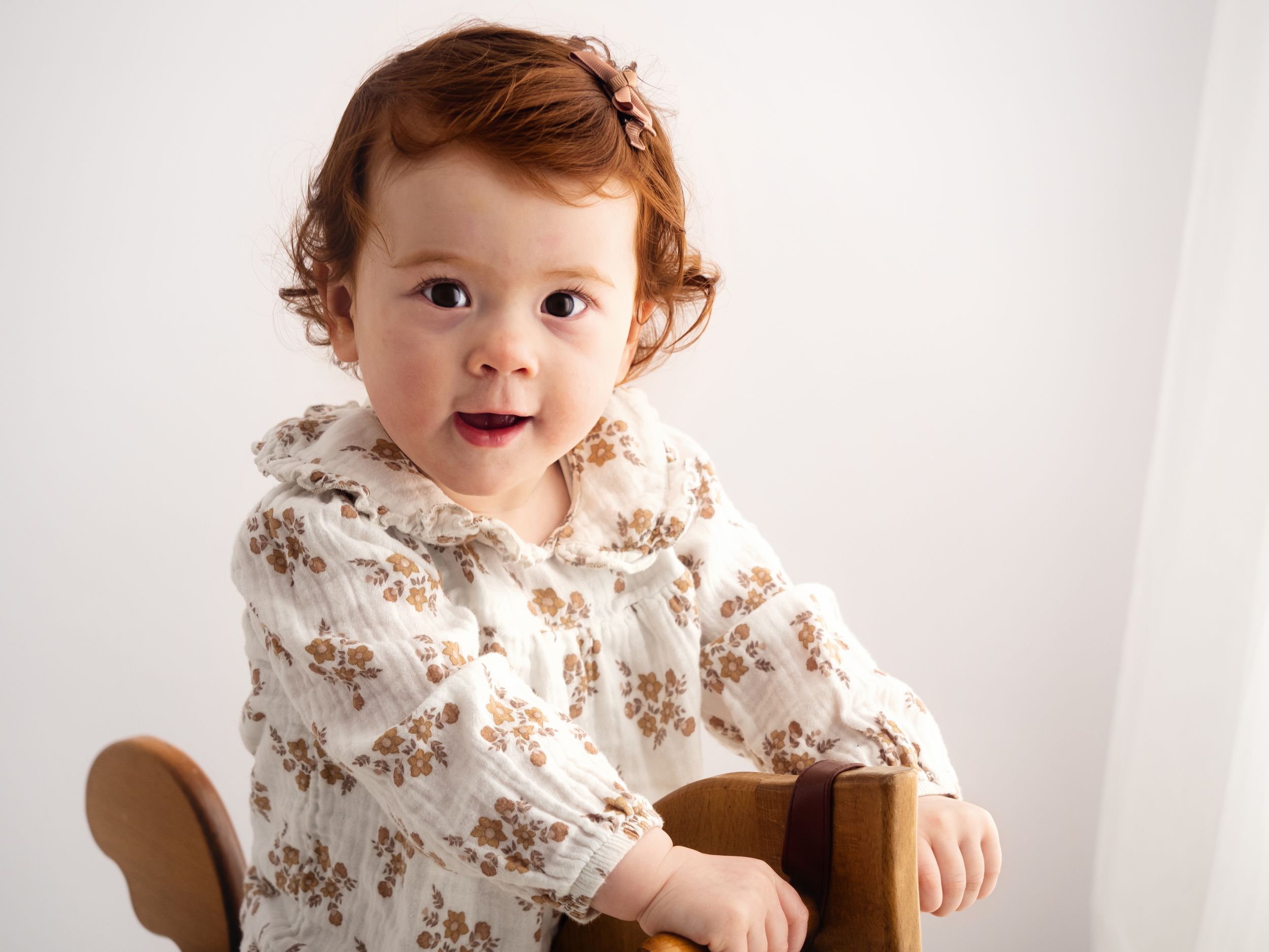 A one year old baby sits on a wooden horse and smiles at the camera during her first birthday photoshoot in Didcot