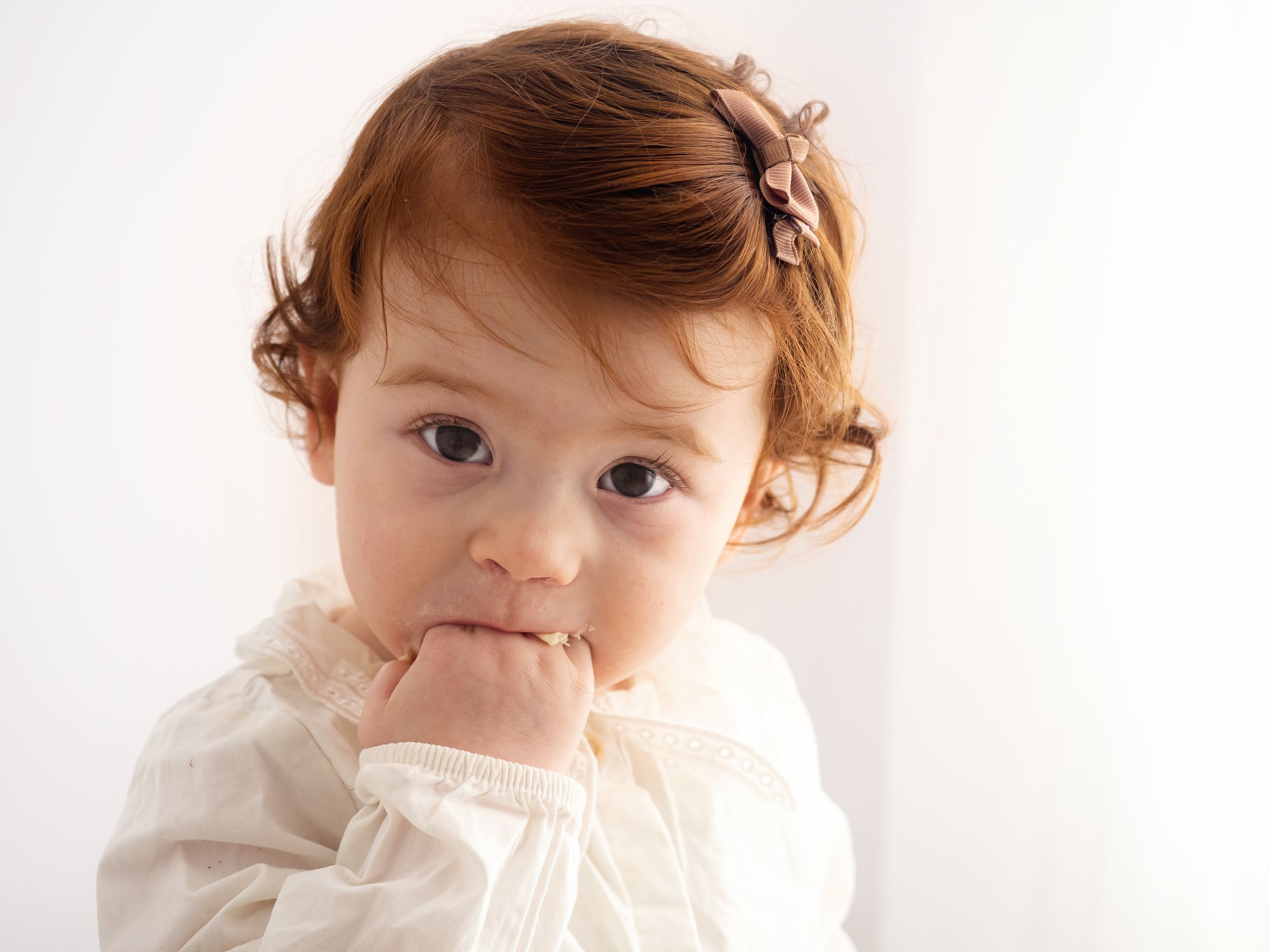 A one year old baby puts her hand in her mouth during a cake smash first birthday photoshoot in Didcot