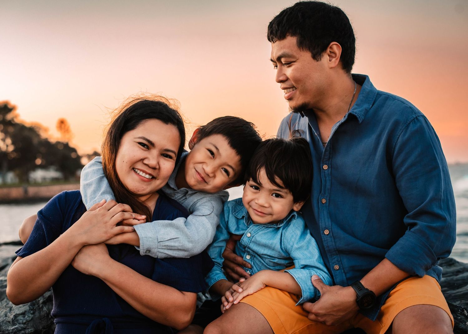 Happy family of four sharing warm embraces and laughter during sunset.