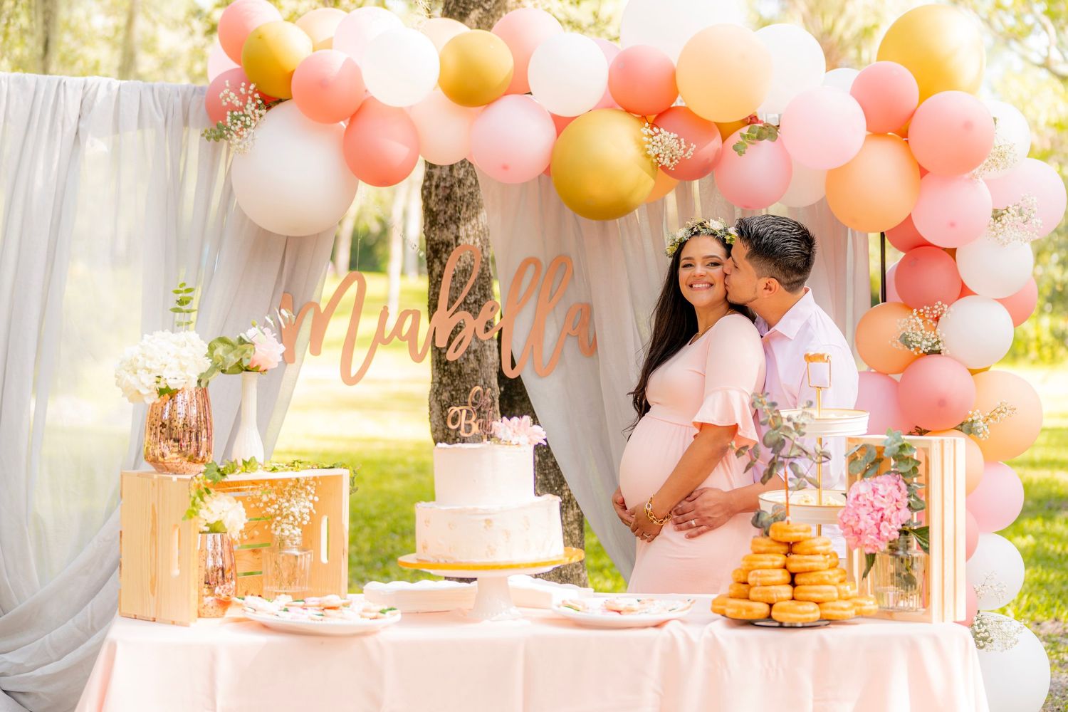Elegant party setup with peach and coral balloon garland and white drapery.