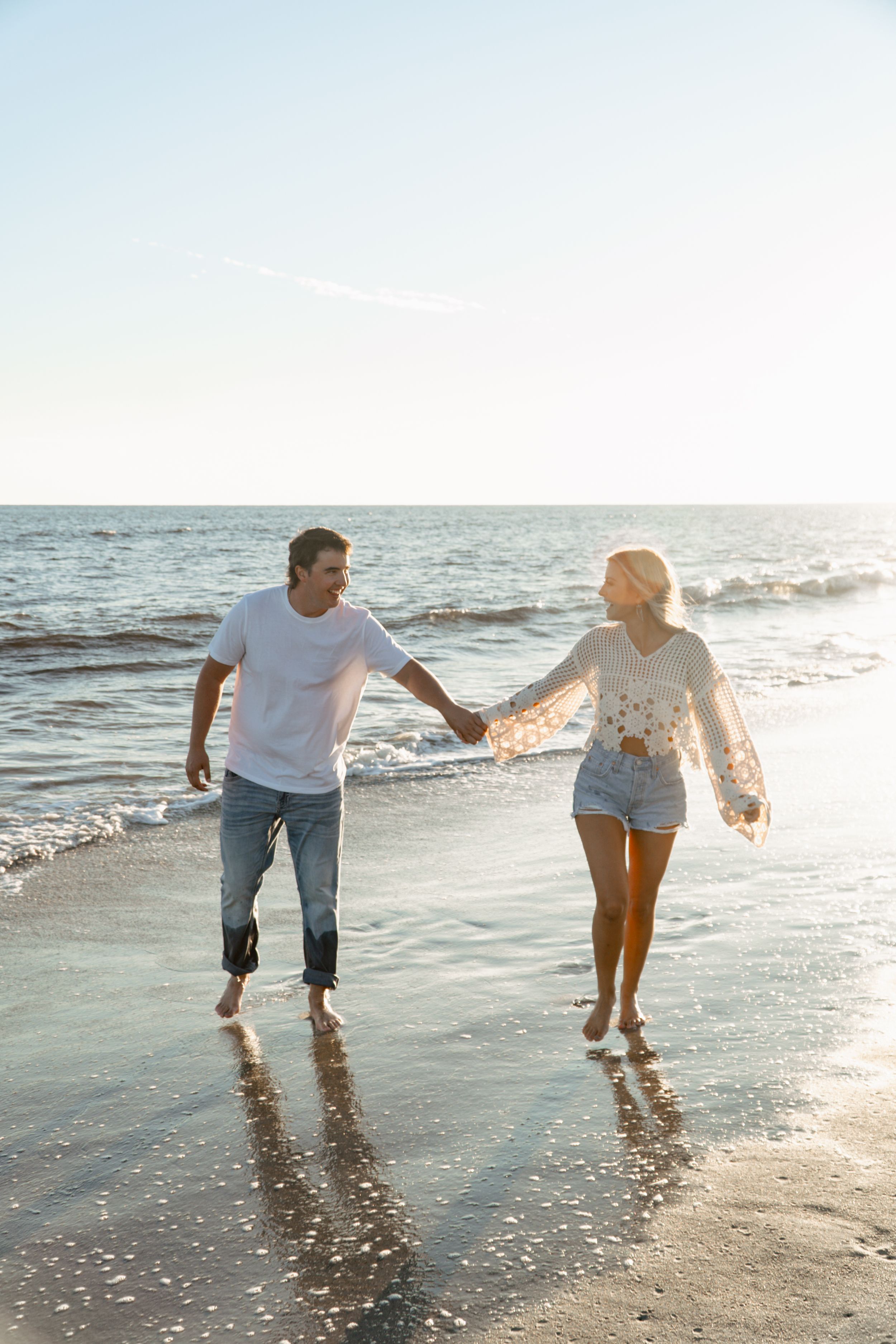 Two people walking hand in hand along the shoreline at sunset.