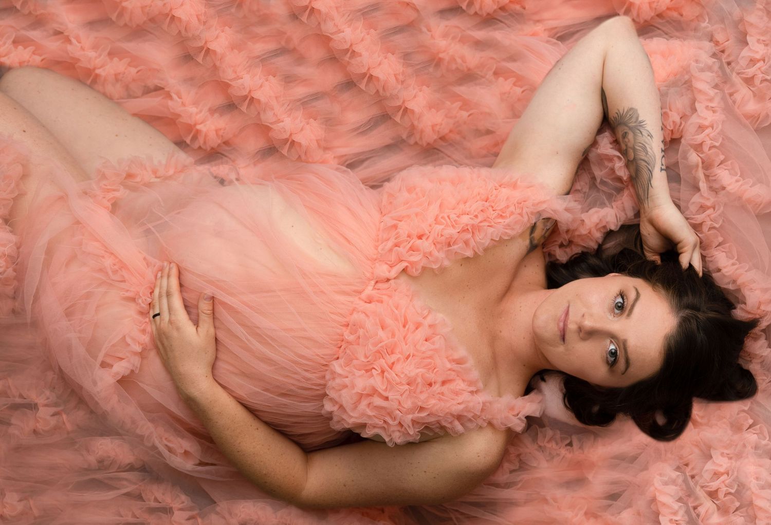 Woman in peach tulle gown poses gracefully on dark background.