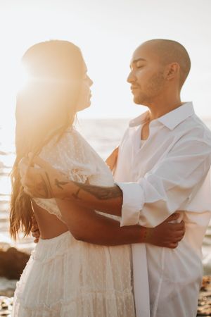 Romantic couple in white clothing sharing tender moments on beach at sunset.