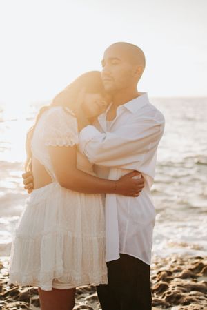 Sun-drenched couple embracing on a rocky beach at golden hour.