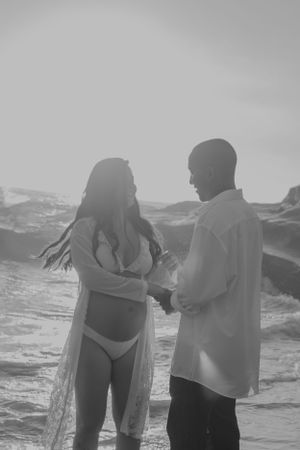 A couple stands together in the ocean waves during sunset.