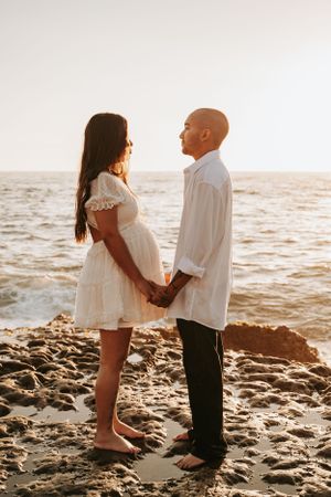 Couple in white clothing sharing intimate moment on rocky beach at sunset.